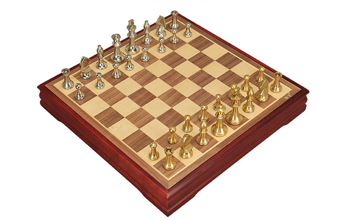 Metal chess set set up on its wooden board, angled view