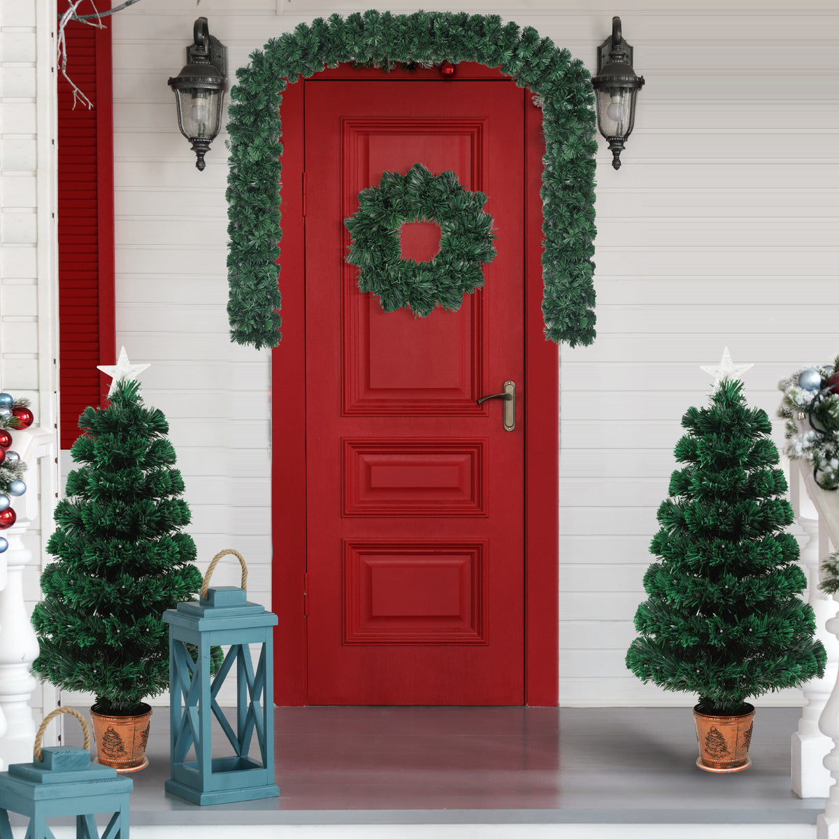 Two potted entrance trees with a wreath and garland around a red door
