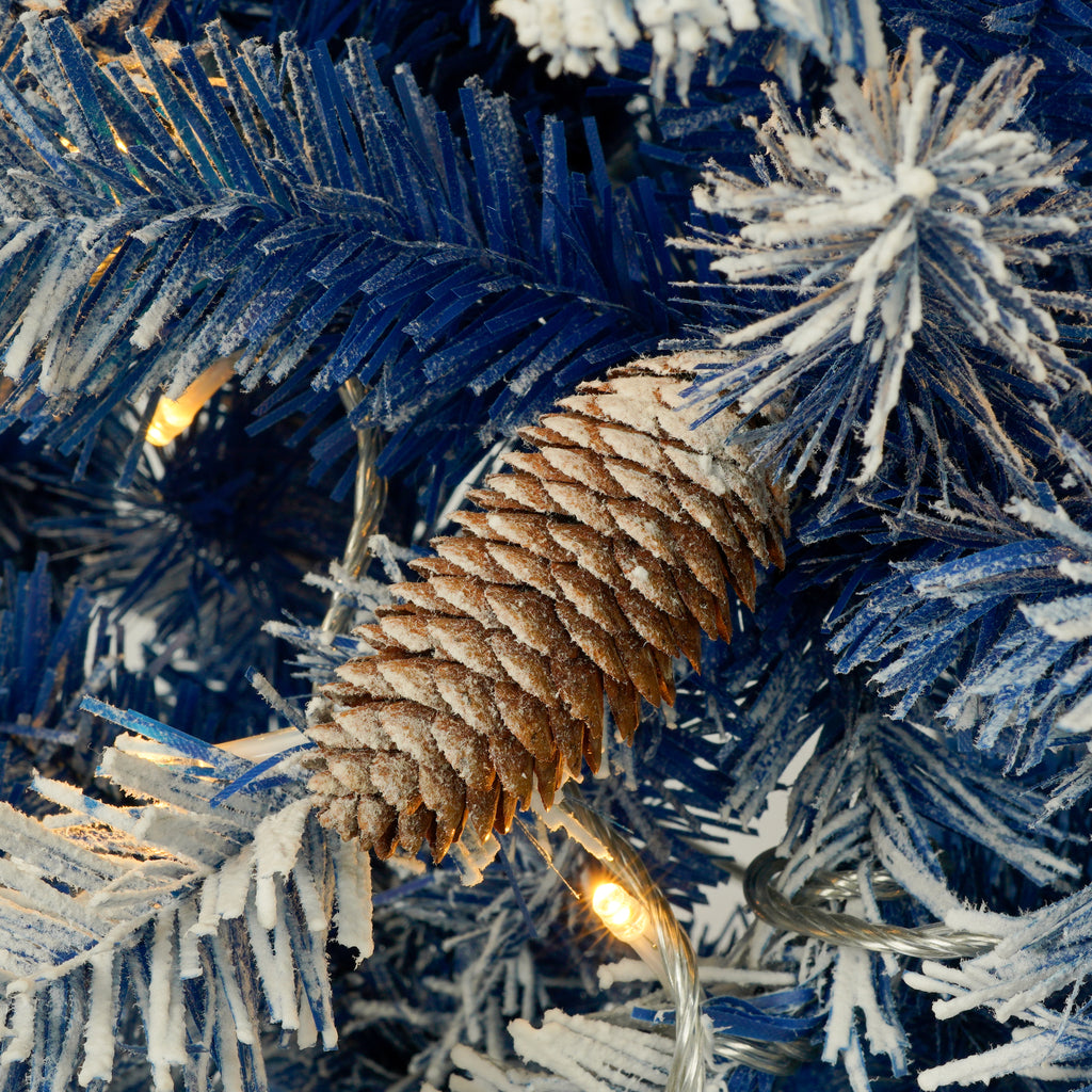 Close-up of blue flocked branches with a pine cone and warm light