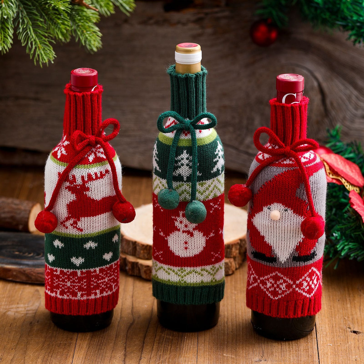 Three knitted Christmas wine bottle covers styled on a wooden table