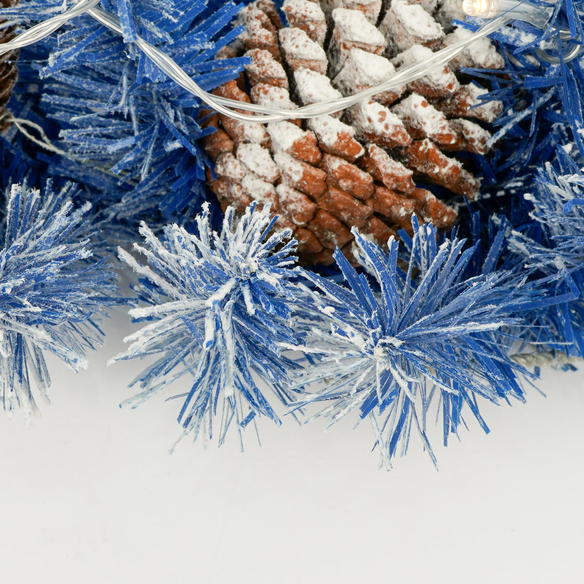 Blue branches with a pine cone and string lights, close-up