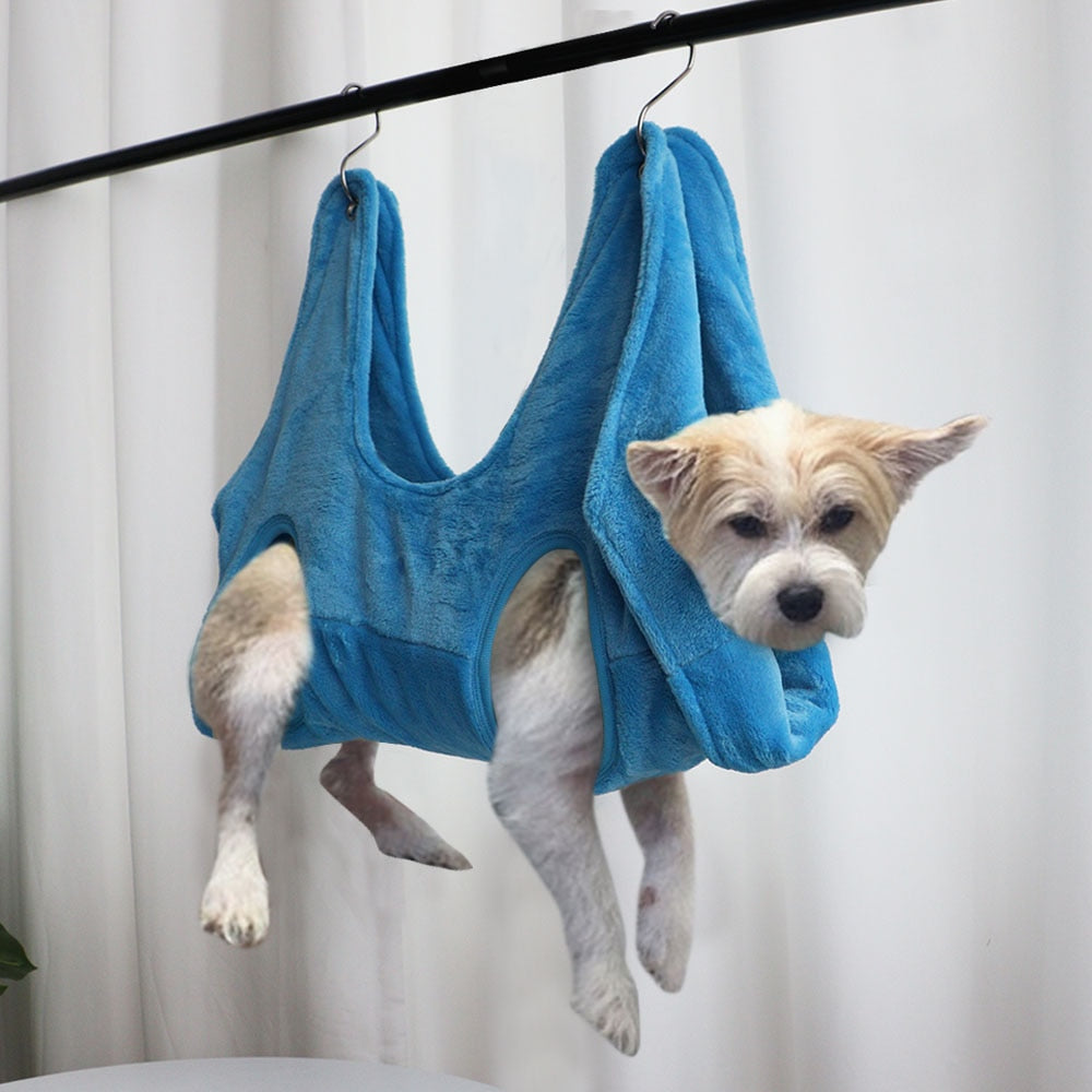 Small dog in a blue pet grooming hammock hanging from a bar