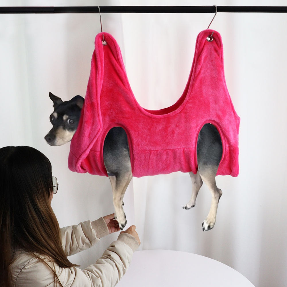 Dog hanging calmly in a pink pet grooming hammock for nail trimming by DealSpark