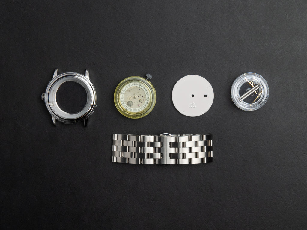 Newton watch kit parts laid out — case, movement, dial and strap