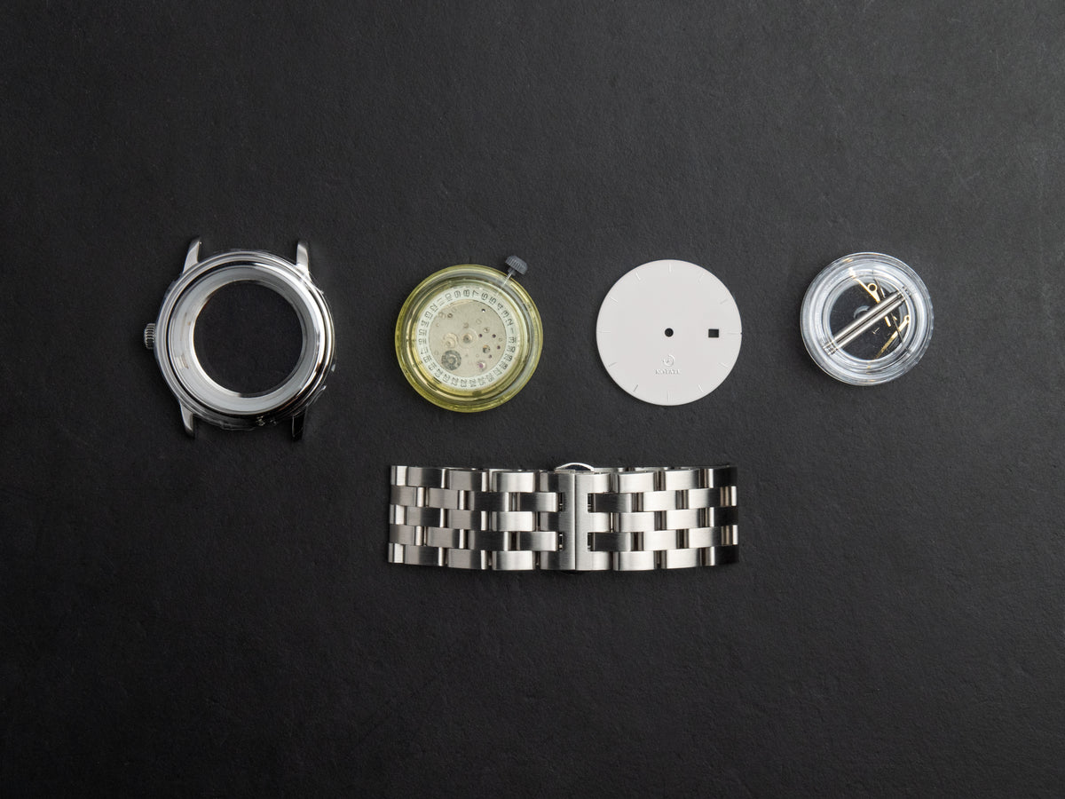 Newton watch kit parts laid out — case, movement, dial and strap